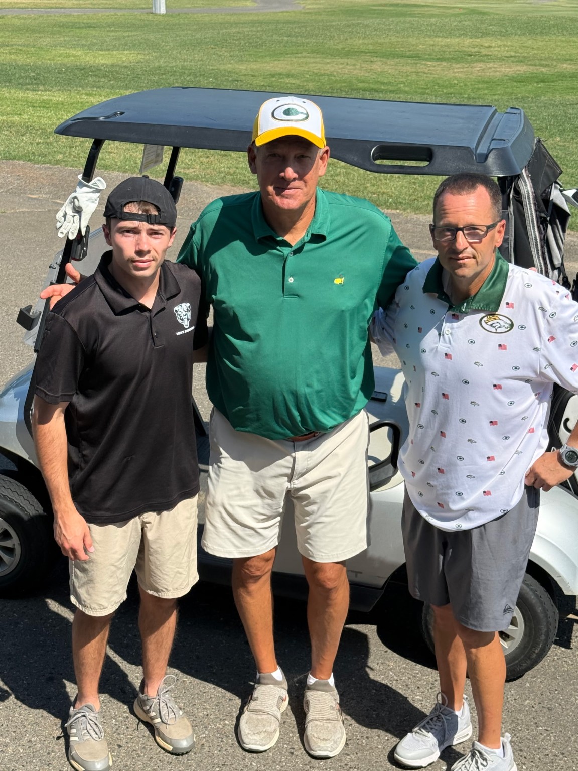 Tournament participants standing by a golf cart
